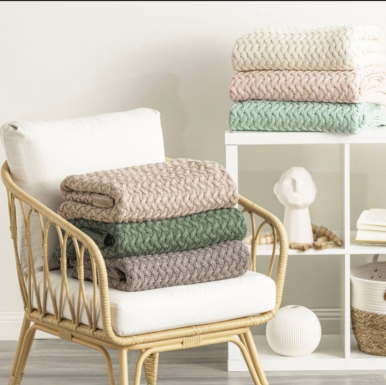 A colourful collection of throw rugs folded on a cane chair. 