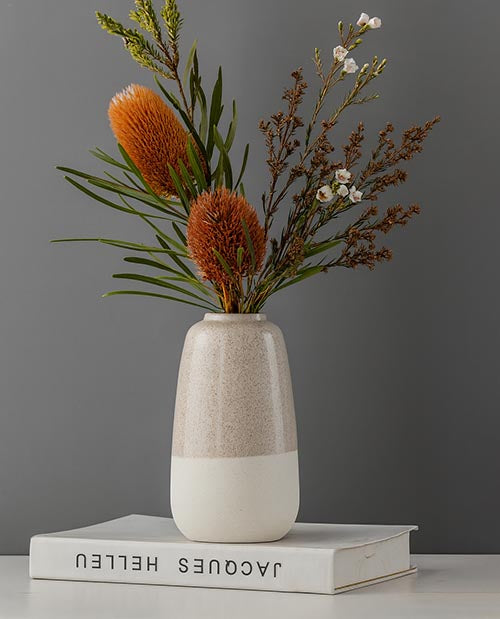 A two tone ceramic vase featuring a bunch of native Australian flowers. 